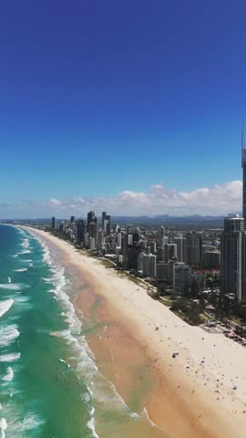Seaside resort and tourism centre district in city of Queensland. Skyline with high.rise buildings along sandy beach and turquoise water. Summer time in Australia. Aerial vertical wide shot.
