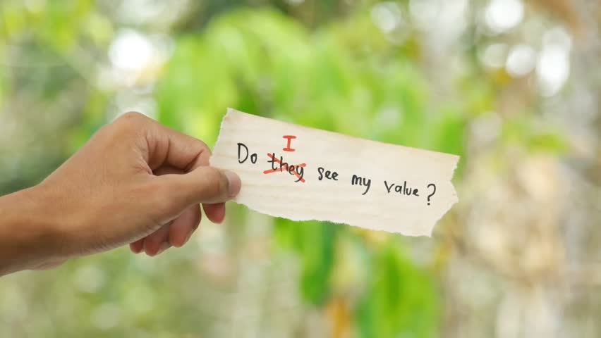 A hand holding a torn paper with the handwritten text Do they see my value? replacing Do I see my value? against a blurred nature background, symbolizing self-worth and questioning