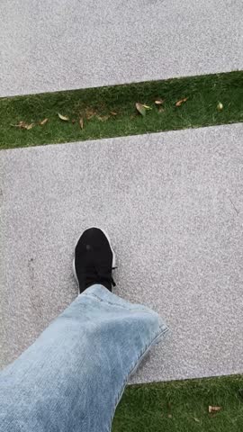 POV top view leg in black sneakers under blue jean stepping on square ceramic tiles under the ground of park. walk and exercise concept. First person view of stepping feet.