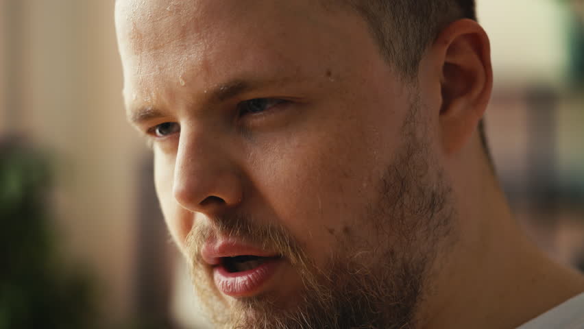 Tired young plus-size man wiping sweat after intense workout, home weight loss