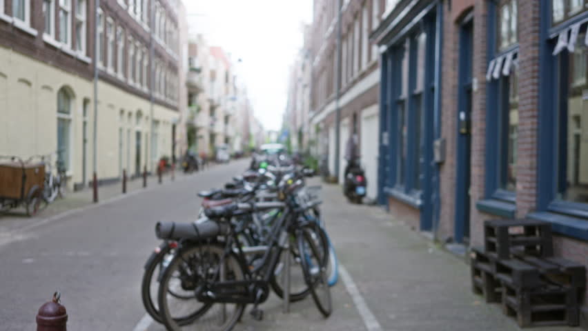 Blurry street in amsterdam with defocused bicycles lined along a narrow alley in a vibrant urban scene showcasing local architecture.