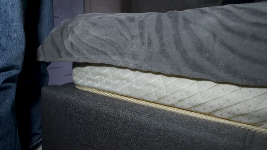 Person hand placing a bundle of US dollar bills hidden under a mattress in a bed storage compartment. Secret savings, hidden cash, financial secrecy, or emergency money