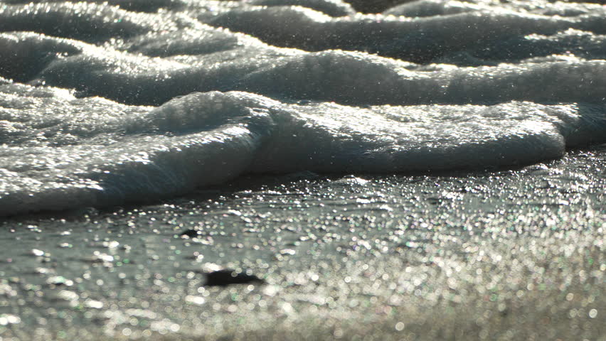 Waves Foam Beach Closeup - Foamy ocean waves crashing on a sandy beach in a close-up shot.