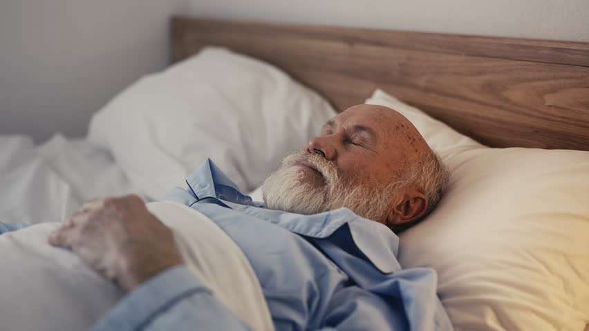 Senior man smiling and stretching hands after waking up, morning routine