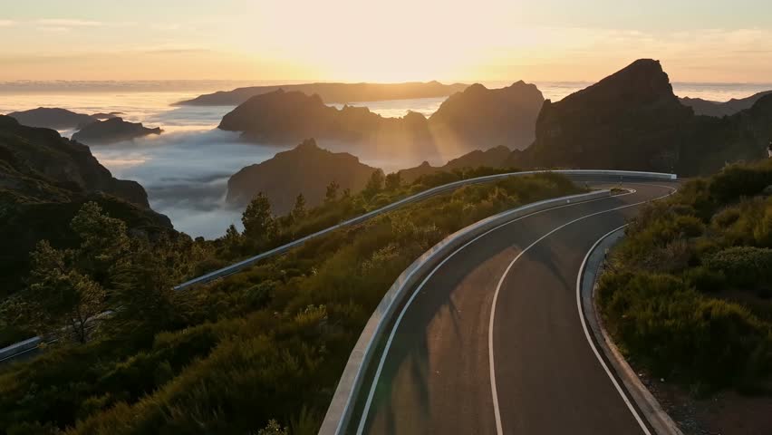 Epic Sunset View in High Mountain Landscape with Motorcycle Driver Riding on Asphalt Road . Pico do Arieiro , Madeira Island . Clouds in the Valley .