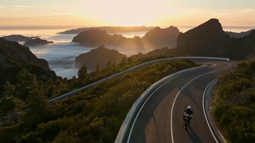 Epic Sunset View in High Mountain Landscape with Motorcycle Driver Riding on Asphalt Road . Pico do Arieiro , Madeira Island . Clouds in the Valley .