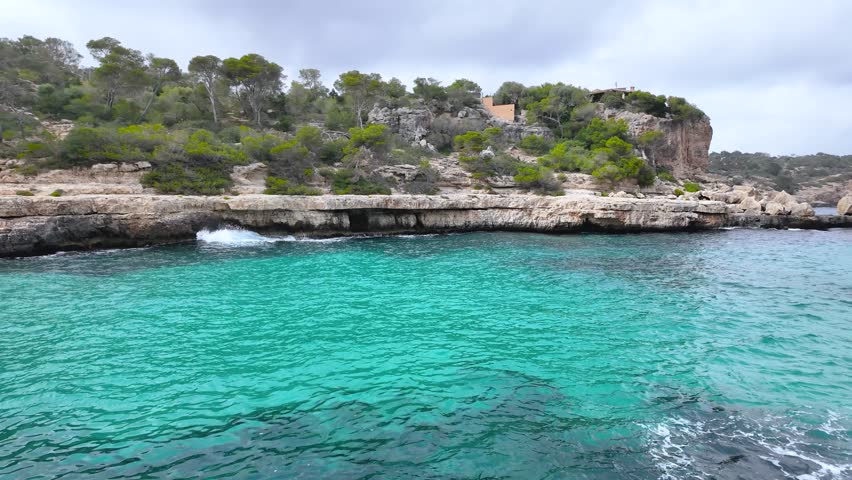 Tranquil turquoise water gently laps the rocky coast of cala llombards, majorca, creating a serene mediterranean seascape