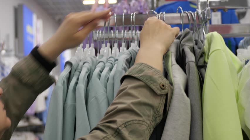 Shopping woman, inspecting hoodie in clothing store aisle, A woman inspects a light blue hoodie in a retail clothing store