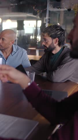 Vertical. Diverse team of professionals engages in a productive meeting, utilizing laptops for data analysis and collaborative discussion in a vibrant, modern office environment