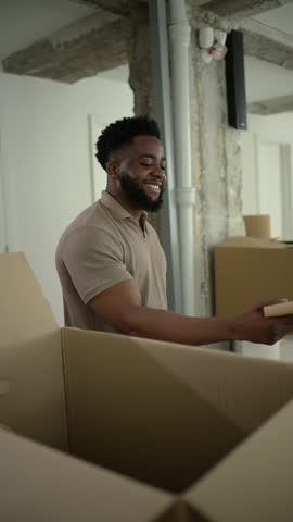 Enthusiastic male homeowner unpacking personal belongings from cardboard box, celebrating new apartment and fresh start with evident joy and positive energy