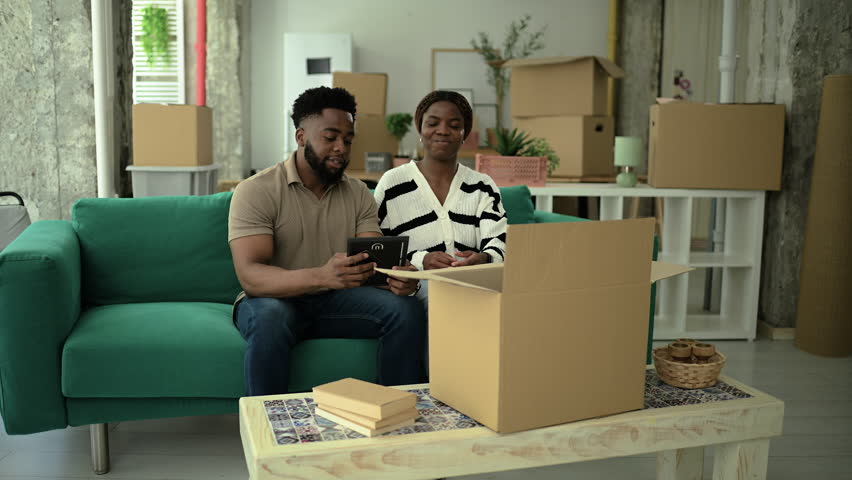 Young african american couple working together, carefully unpacking cardboard boxes, creating home in bright, modern apartment, sharing moment of excitement and new beginnings
