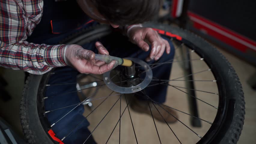 Professional mechanic in a workshop repairs a mountain bike, focusing on the hub and bearings. Wearing workwear, he provides expert service, lubrication, and maintenance to ensure smooth performance. 