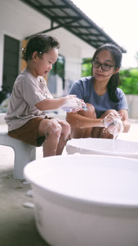 Cute toddler helping his mom wash socks with soap suds during laundry time. A sweet and candid parenting moment showing family bonding, early responsibility, and everyday love.