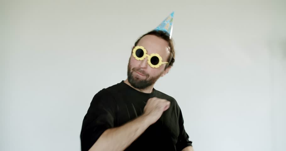 Excited man wearing a birthday hat and funny glasses dances and points at the camera. He is having a blast celebrating his birthday, enjoying the festive atmosphere and sharing his joyful spirit.