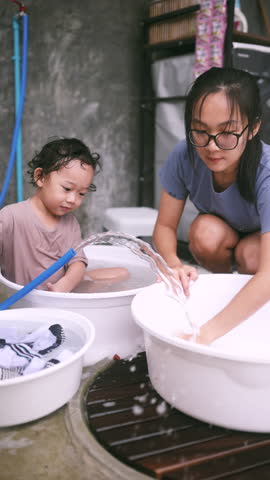 Cheerful toddler sitting in a washbasin while helping his mom do laundry. A funny and heartwarming moment capturing parenting life, playful mischief, and daily family chaos.
