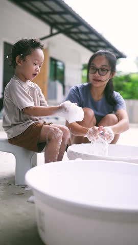Cute toddler helping his mom wash socks with soap suds during laundry time. A sweet and candid parenting moment showing family bonding, early responsibility, and everyday love.