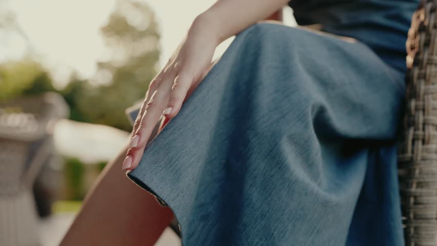 A close-up image of a woman's hand gently resting on a denim dress. The background shows an outdoor setting with natural light. The image evokes a sense of tranquility and femininity.