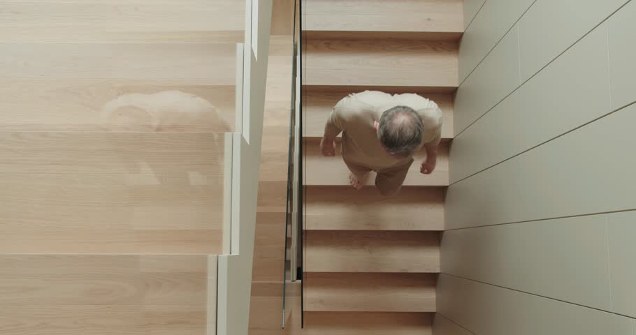 Senior Man Carefully Descending Wooden Stairs in Modern Home. Overhead view of an elderly man cautiously walking down wooden stairs, capturing the essence of aging and home safety.