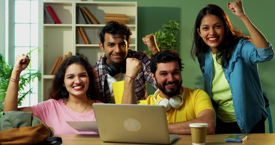 Celebrating success after completing assignment, Indian college students using laptop, books, notes while studying in friendly atmosphere at library, showing positive gestures, thumbs up fist bumps