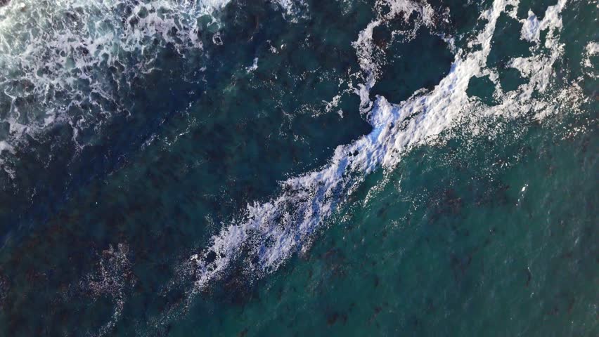 Top-down aerial shot of waves crashing against the rocky shores of Bluff Cove during golden hour, Palos Verdes Estates, California