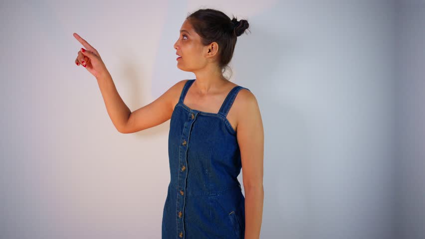 Stylish promoter highlights object by pointing up, Female presenter gesture upward showing product landmark, Model motion high suggesting fresh produce, Woman introduce the goods with flair, Signaling
