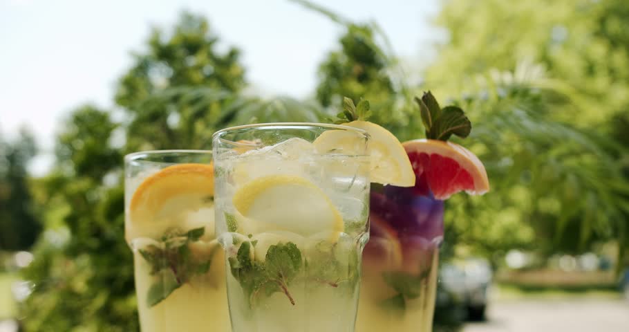 Refreshing summer soft lemonade drinks with lemon, citrus, orange, grapefruit, mint, water and ice rotating on natural outside background. Refreshing soft drink Lemon. Glass of lemonade.