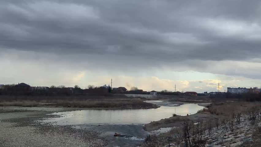 Cloudy skies over a tranquil river landscape during late afternoon near a small town