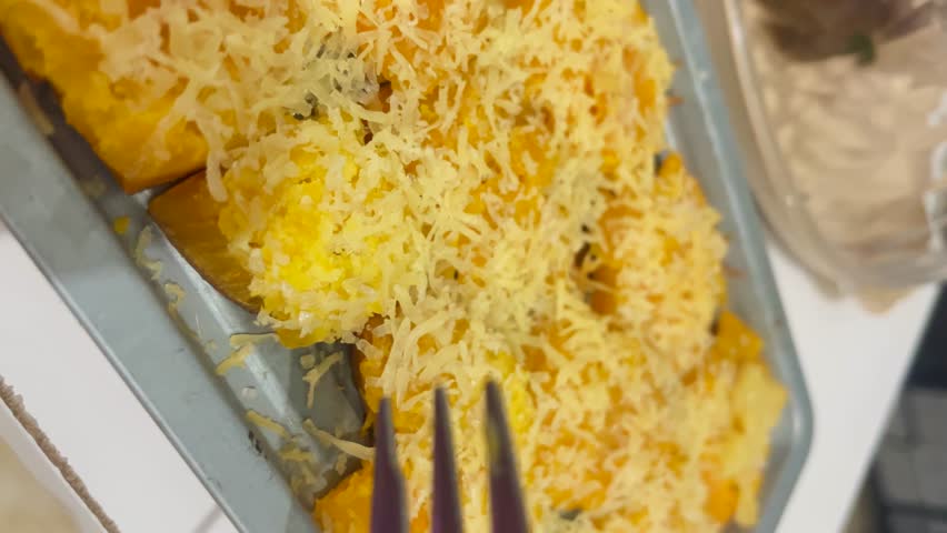 A close-up of Oven-Baked Yellow Sweet Potato in an oven tray, topped with melted grated cheese, golden and ready to be tasted with fork