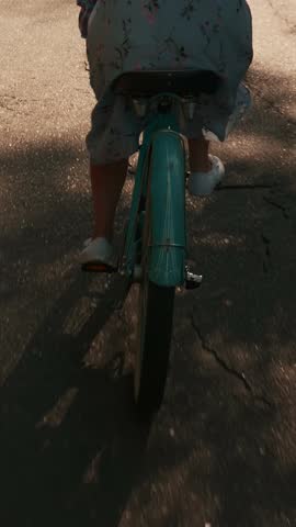 Young girl in hat and summer dress is riding vintage bicycle at sunset. Woman cycling on old bike in park at summer, back follow shot. Vertical video