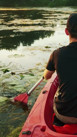 Fitness muscular man is sailing in kayak on river at sunset. Sport rowing. Sportive male tourist is floating in canoe and practicing paddling. Vertical video