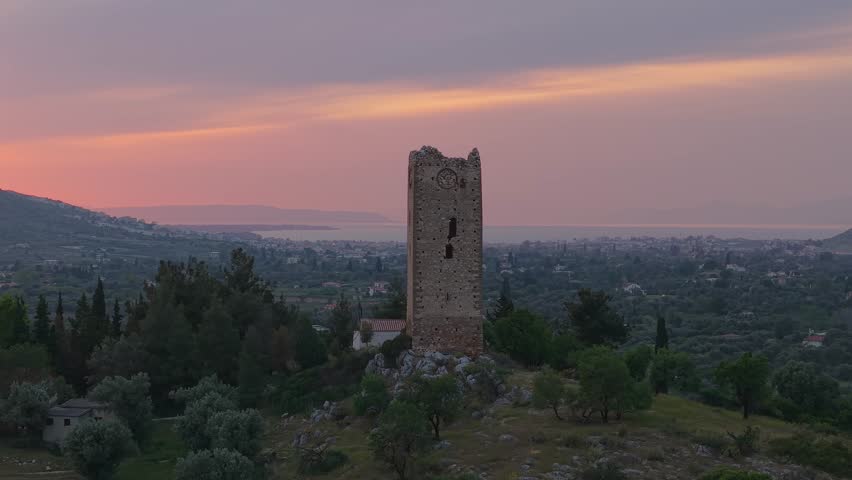 Drone Orbit Around Ancient Stone Observation Tower at Twilight with Orange Sky and Chalkida in the Background