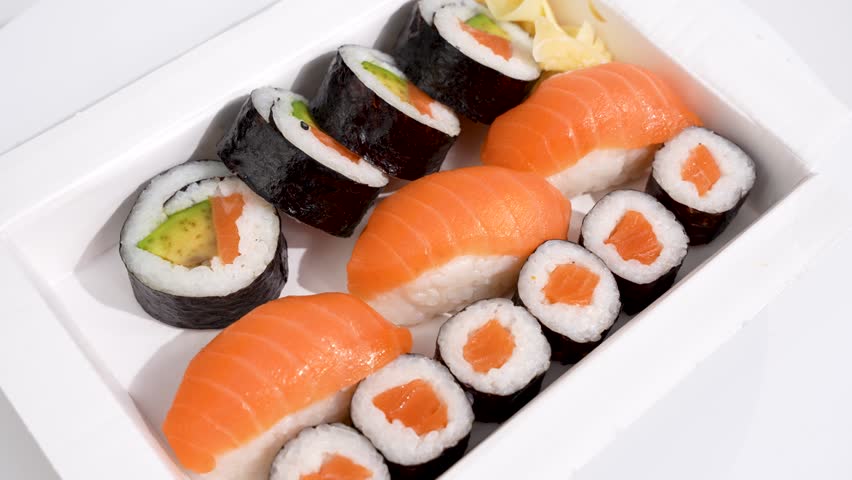 Salmon and avocado sushi box rotates on white background. Fresh salmon and avocado sushi is presented appetizingly in a white box. The combination of nigiri and maki impresses with its color and fresh - Powered by Shutterstock - Get 15% off with code: PIKWIZARD15