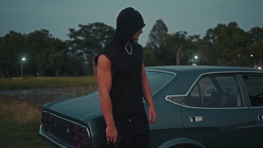 A Stylish Young Man Posing Confidently Next to a Vintage Car During the Dusk Hours