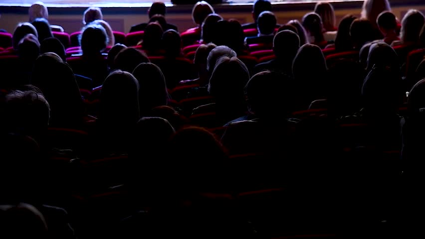 People are enjoying the singer's performance on stage. They listen to music at a concert while sitting in the auditorium