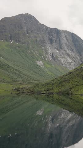 Explore a serene landscape in Norway, where towering mountains meet a tranquil lake.