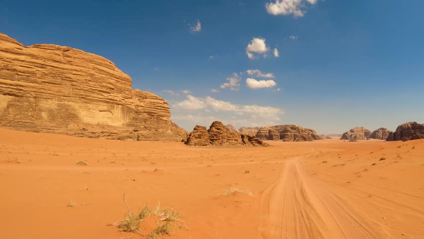 Driving perspective view through the vast desert landscape with towering sandstone rock formations under a clear blue sky in Wadi Rum, Jordan.