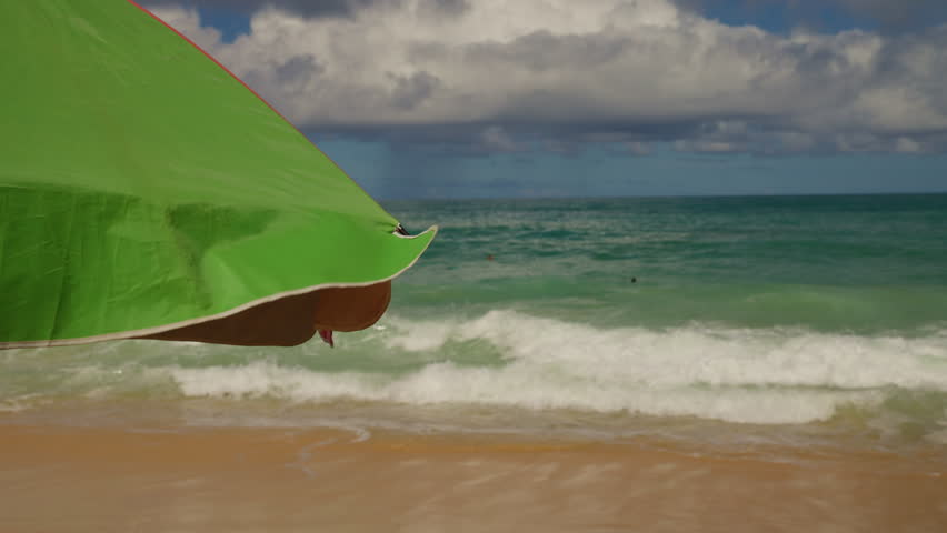 Vibrant Green Beach Umbrella Adjacent to Serene Ocean Waves and Cloudy Skies, Capturing a Relaxing Coastal Scene in Two Frames