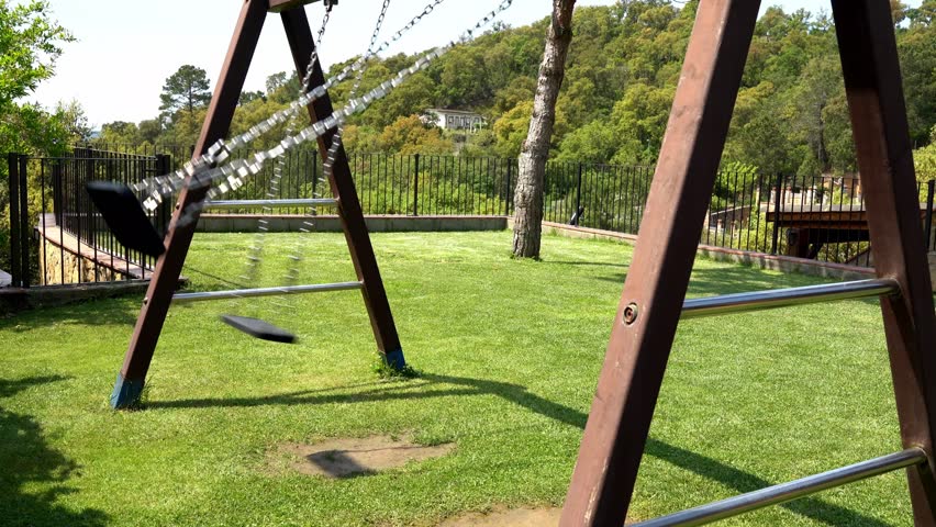 Vintage swing set gently moving in abandoned park, capturing nostalgic childhood moments with serene, repetitive motion against peaceful green landscape