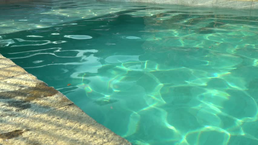 Tranquil turquoise swimming pool surface creating soft light reflections, showcasing pristine water with gentle rippling and serene ambiance during bright daylight