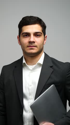 Professional man in business suit smiles confidently while holding a laptop and giving a thumbs up