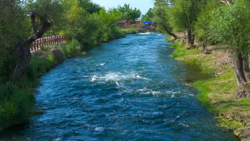 Blue river flowing gently through green lush landscape. Pristine blue river gently flowing through lush green landscape, showcasing vibrant vegetation and serene natural scenery under bright sunlight