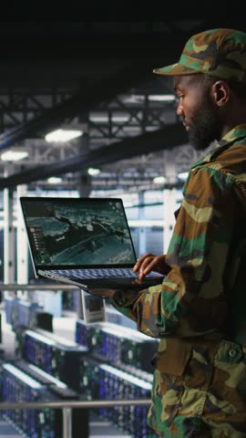 Vertical video Military technician in data center monitoring warfare drone telemetry on laptop dashboard. IT specialist in army server room using tactical interface on notebook to support aerial