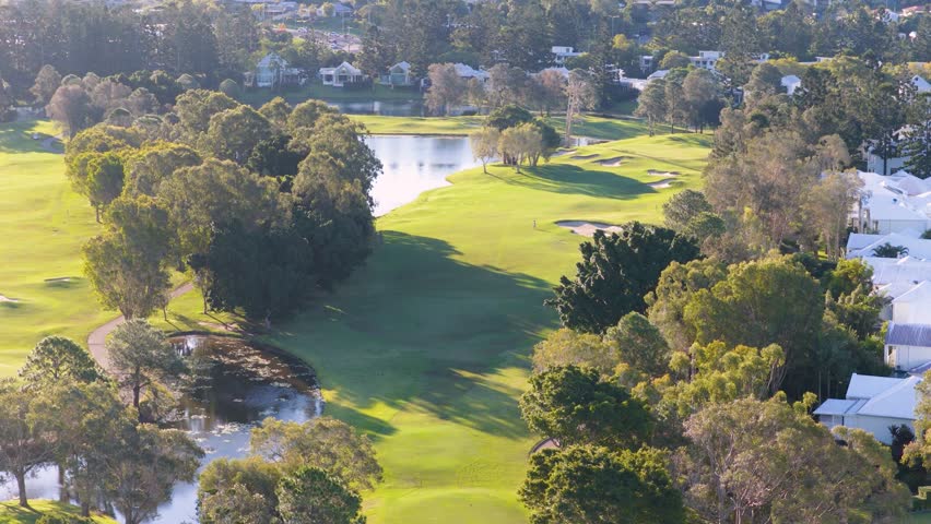 Drone footage captures a serene golf course with lush greenery and water features under bright sunlight