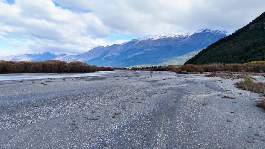A tranquil river flows through a mountainous landscape under a cloudy sky, showcasing natural beauty and serene wilderness