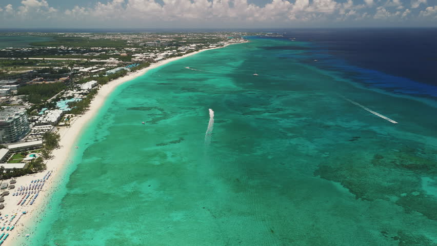 High-altitude aerial follow of a boat driving through the beautiful blue Caribbean water along Seven Mile Beach, Grand Cayman