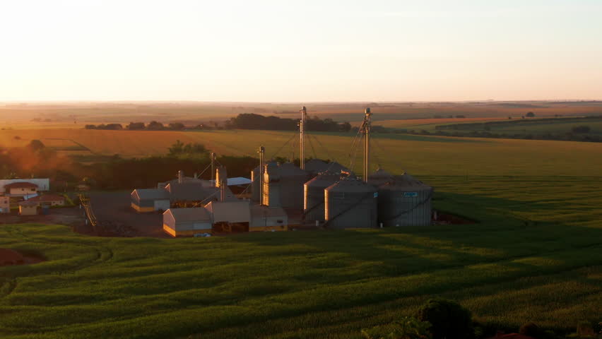 Drone aerial landscape of wheat grain silo factory warehouse facility with tanks and afternoon sunset over valley in industrial countryside farmland in Brazil South America industry agribusiness.