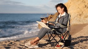 Stylish woman in business attire with loose tie sitting at water edge against backdrop of sea waves rolling onto sandy shore, working on laptop and enjoying glass of wine far from chaos of city life - Powered by Shutterstock - Get 15% off with code: PIKWIZARD15