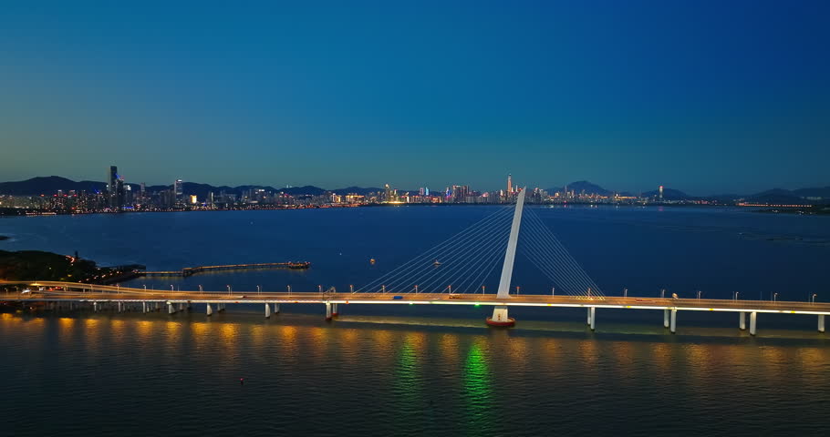 Aerial shot of an illuminated modern bridge spanning across the bay with city skyline at night in Shenzhen, China.