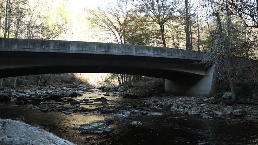 Static shot of a concrete bridge spanning a rocky forest river in the Great Smoky Mountains.
