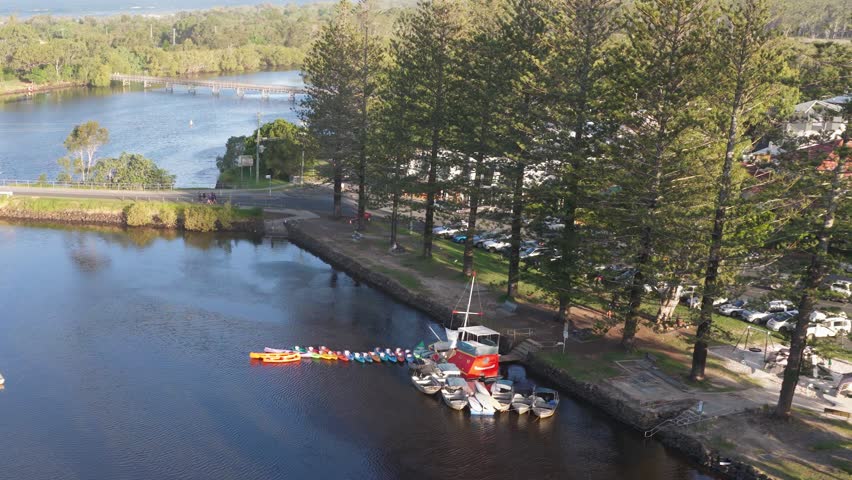 Drone footage captures boats docked along Brunswick River, surrounded by lush trees and calm waters under clear skies